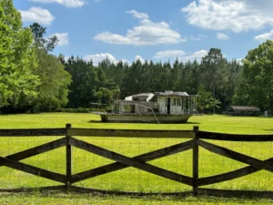 Old, abandoned boat in a grassy field with trees in the background