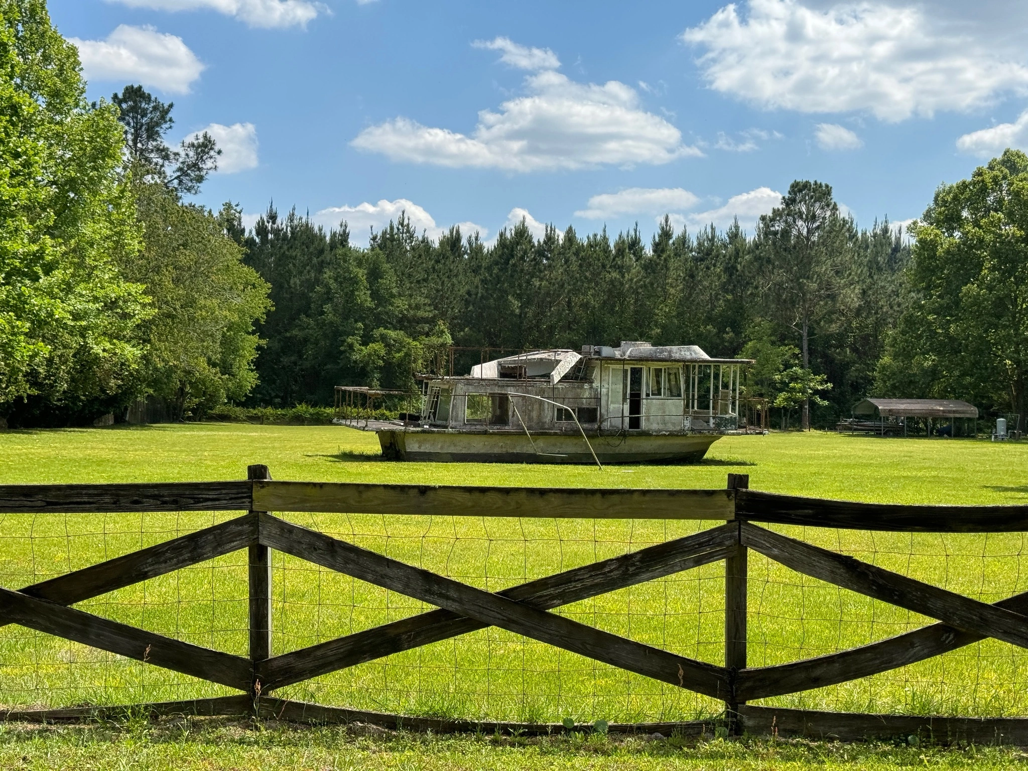 Old, abandoned boat in a grassy field with trees in the background